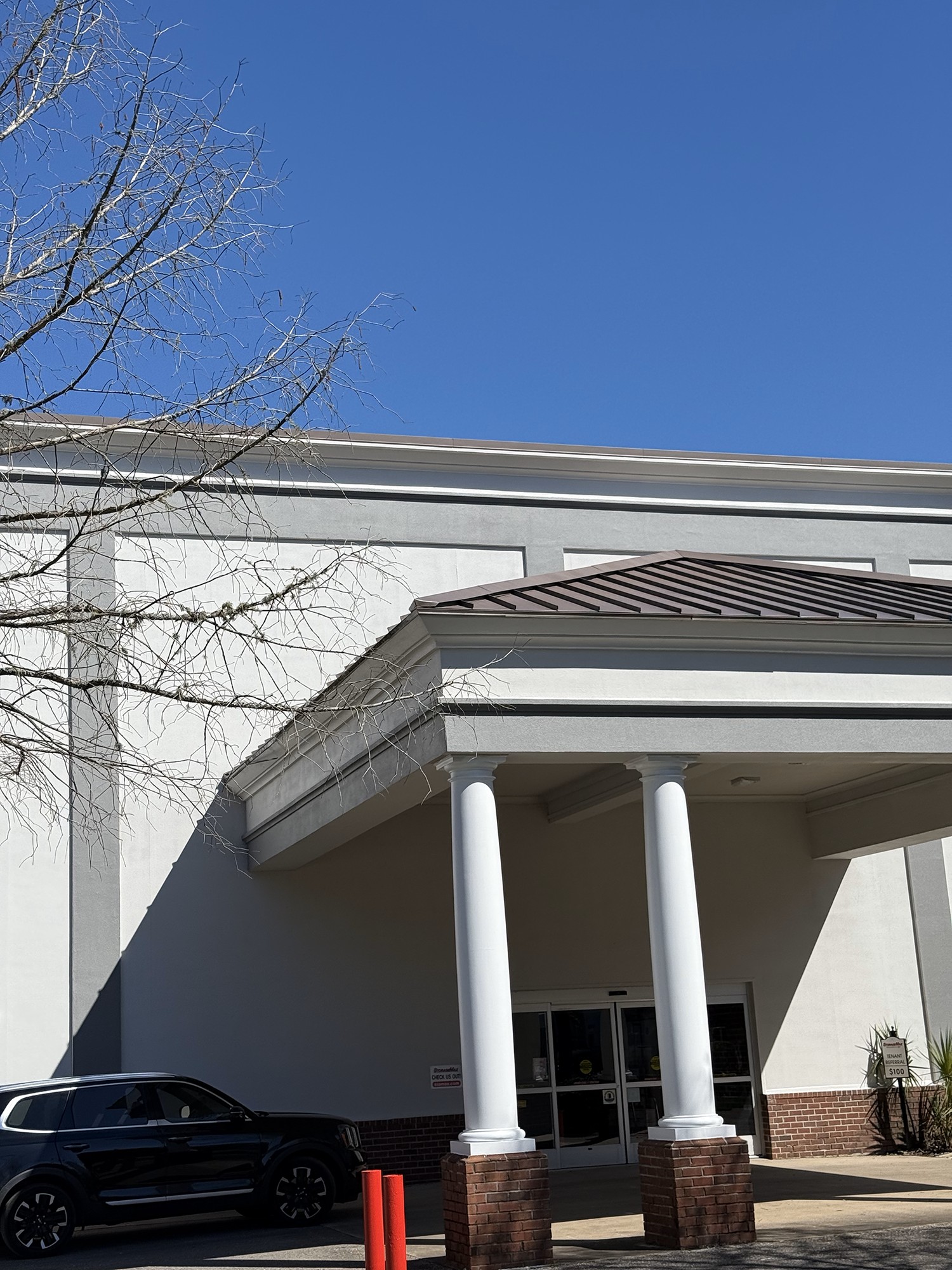 White stucco building entrance with columns and a brown metal roof